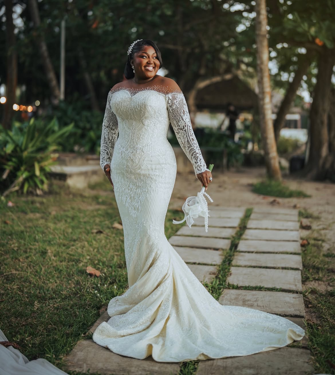 Nollywood actress Blessing Obasi Nzediegwu smiling in off-the-shoulder Prudential pearl lace wedding gown with calla lily bouquet.