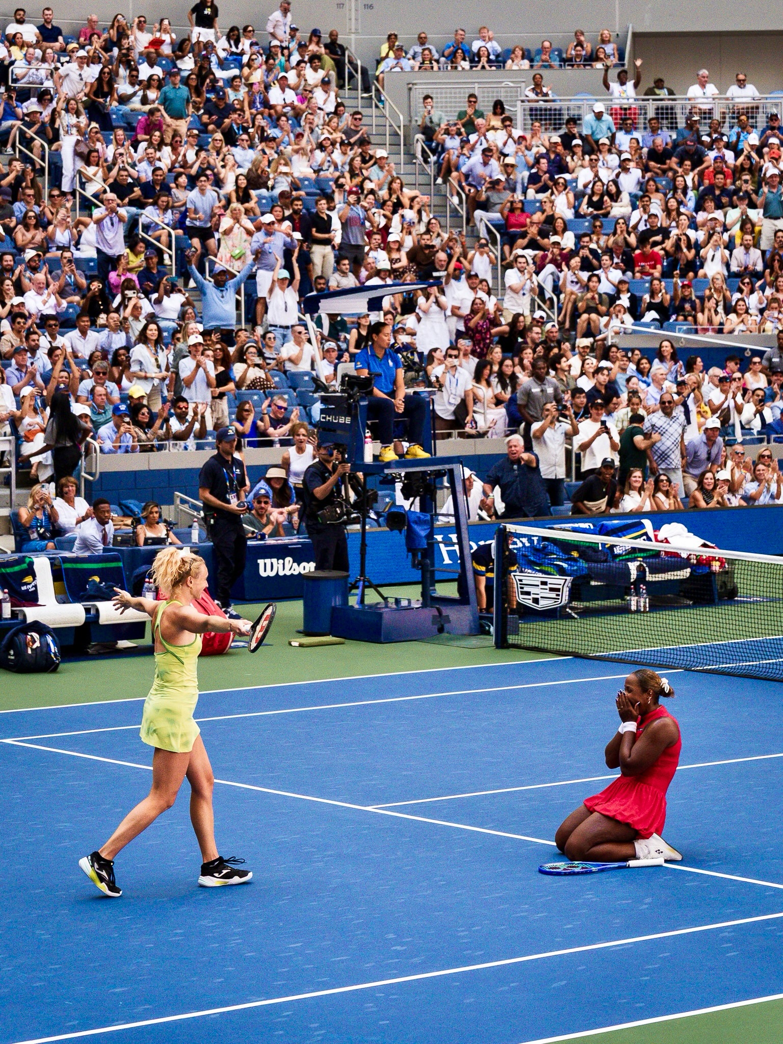 Taylor Townsend on knees covering face in joy as Katerina Siniakova walks toward her on court.