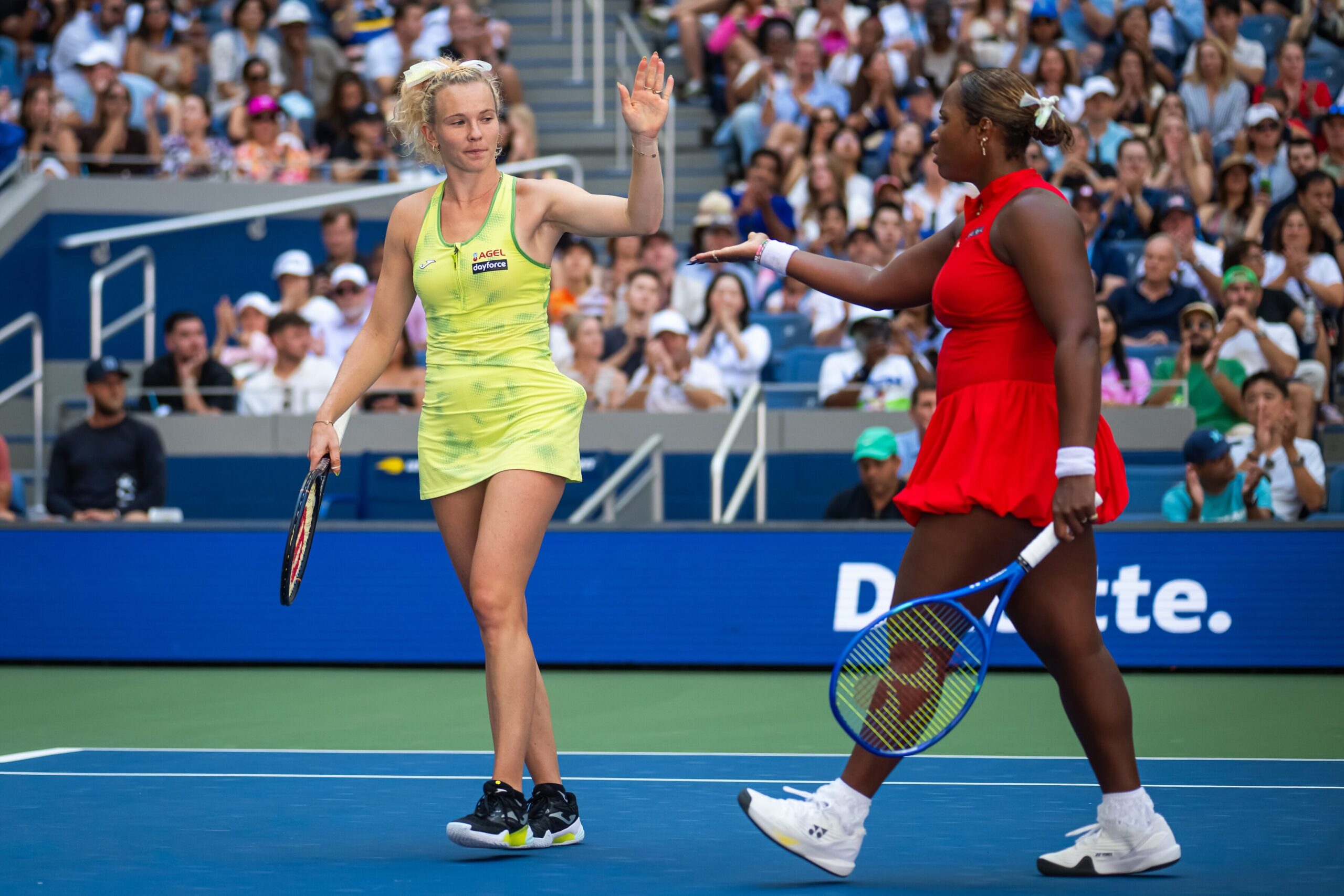 Katerina Siniakova in lime dress high-fiving Taylor Townsend in red dress on tennis court.