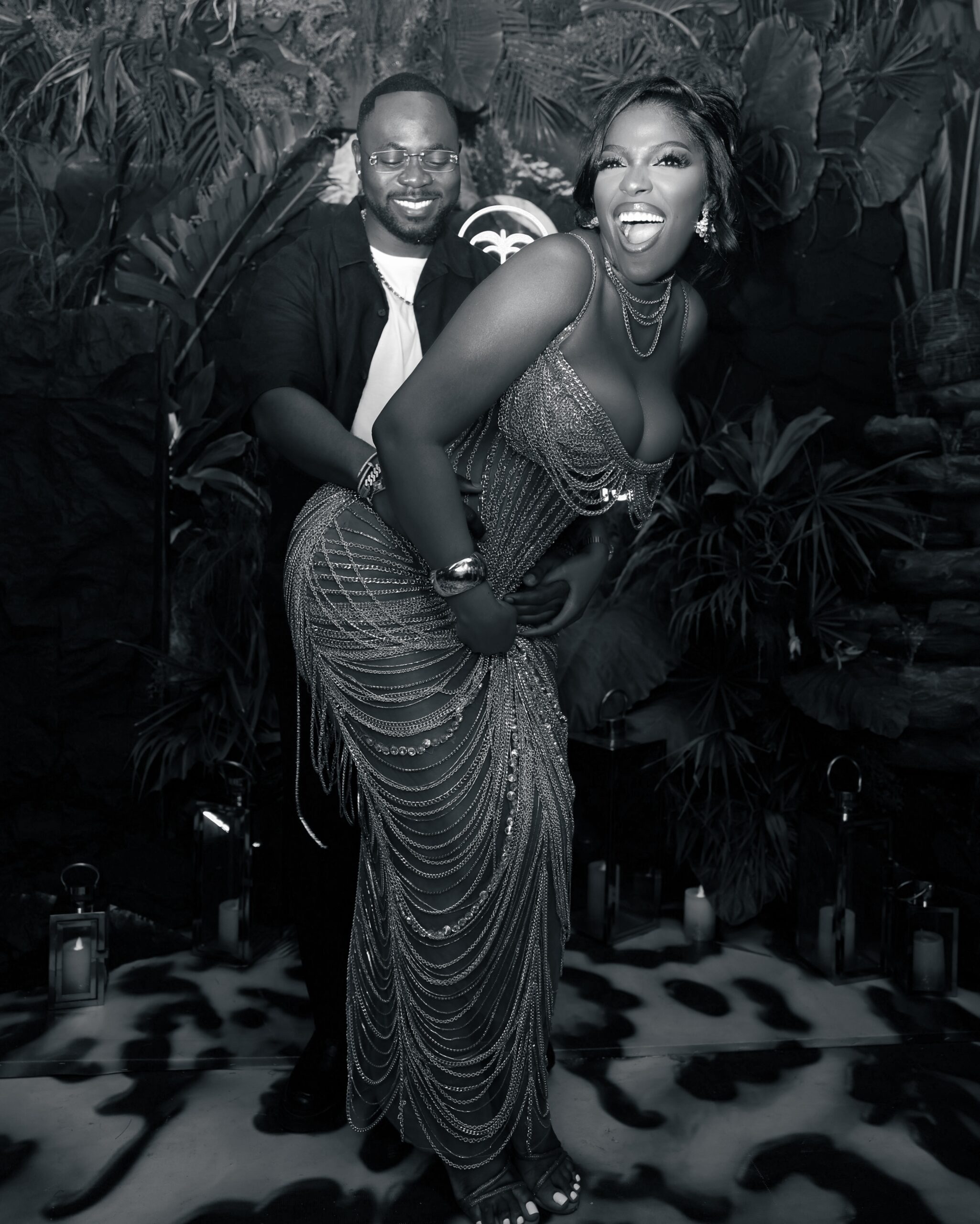 Hilda Baci in a floor-length metallic layered dress laughing alongside Damilola Akinwunmi