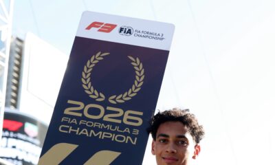 Ugo Ugochukwu holding the official 2026 FIA Formula 3 Champion board draped in the American flag.