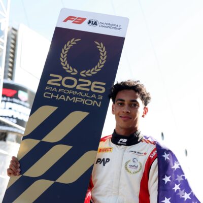 Ugo Ugochukwu holding the official 2026 FIA Formula 3 Champion board draped in the American flag.