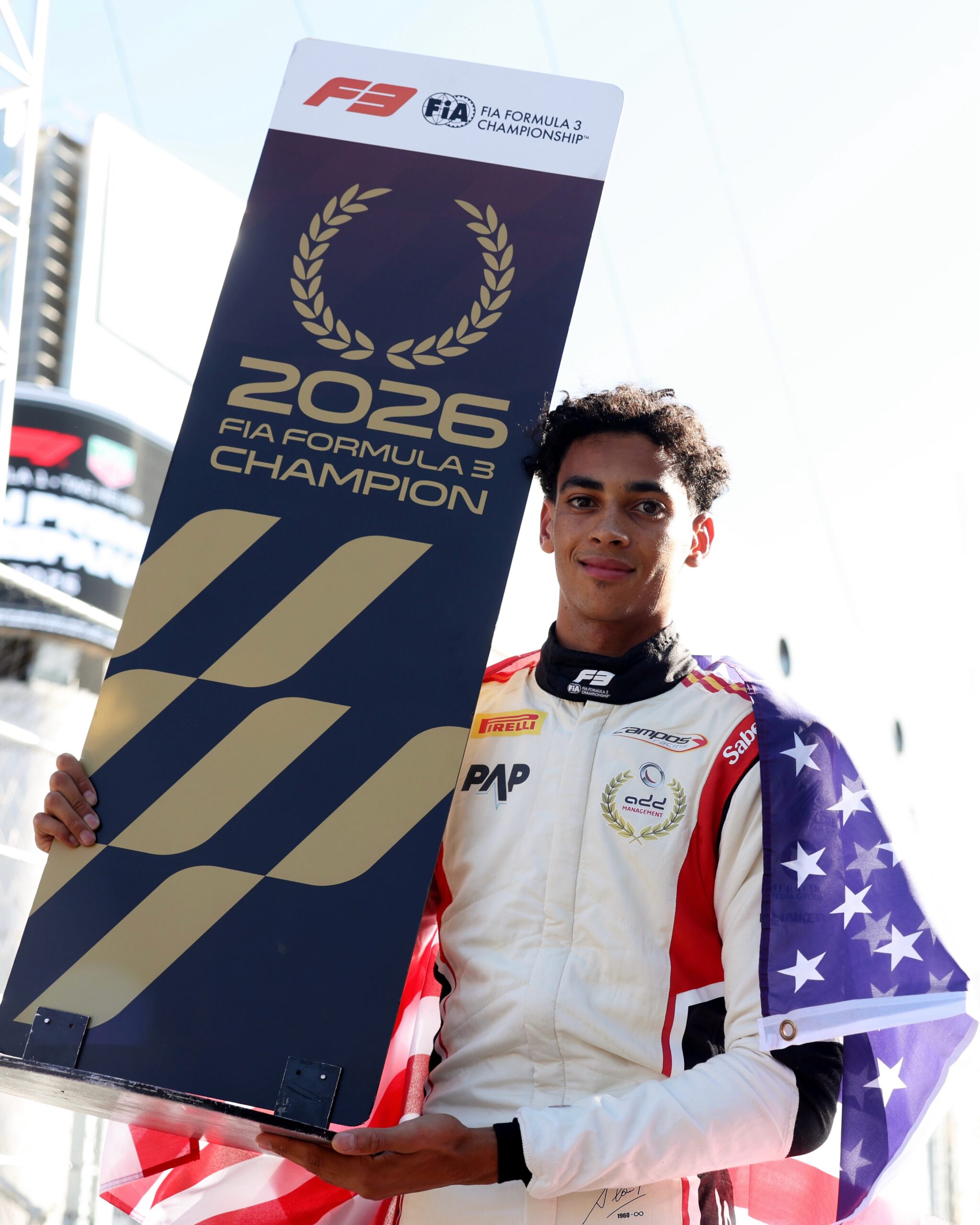 Ugo Ugochukwu holding the official 2026 FIA Formula 3 Champion board draped in the American flag.