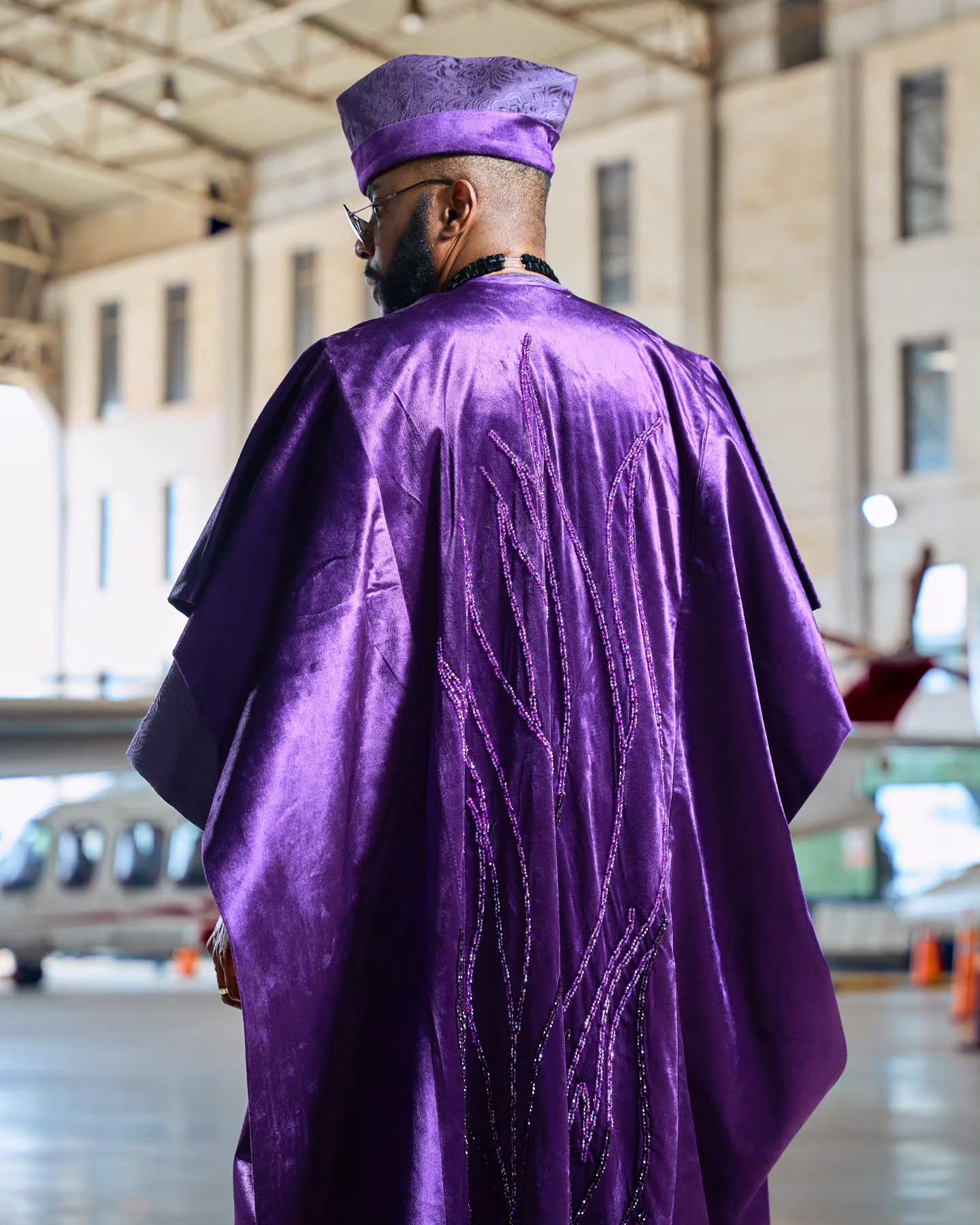 Ebuka Obi-Uchendu facing away in a purple velvet agbada by D29 Africa displaying beaded embroidery down the back.