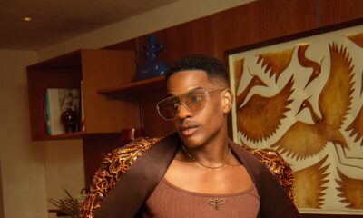 Denola Grey in a brown ribbed tank top with gold bee motifs under a draped sequined jacket with satin lapels for Onalaja SS27 at London Fashion Week