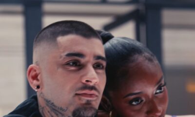 Ayra Starr resting her arm on Zayn Malik's shoulder as he wears a dark embroidered bomber jacket with neck tattoos visible.