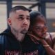Ayra Starr resting her arm on Zayn Malik's shoulder as he wears a dark embroidered bomber jacket with neck tattoos visible.