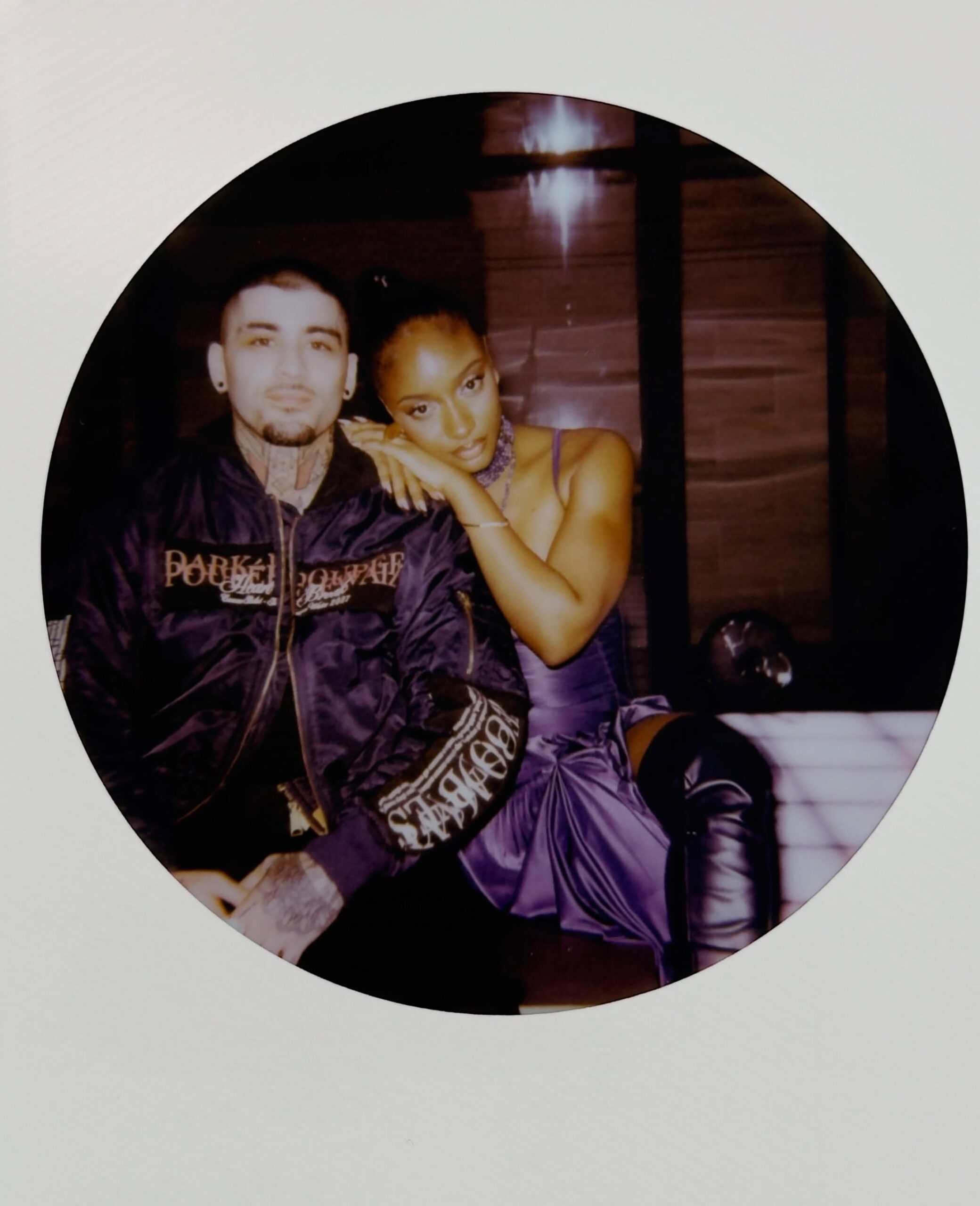 Ayra Starr leaning her chin on Zayn Malik's shoulder in a circular polaroid picture from set.