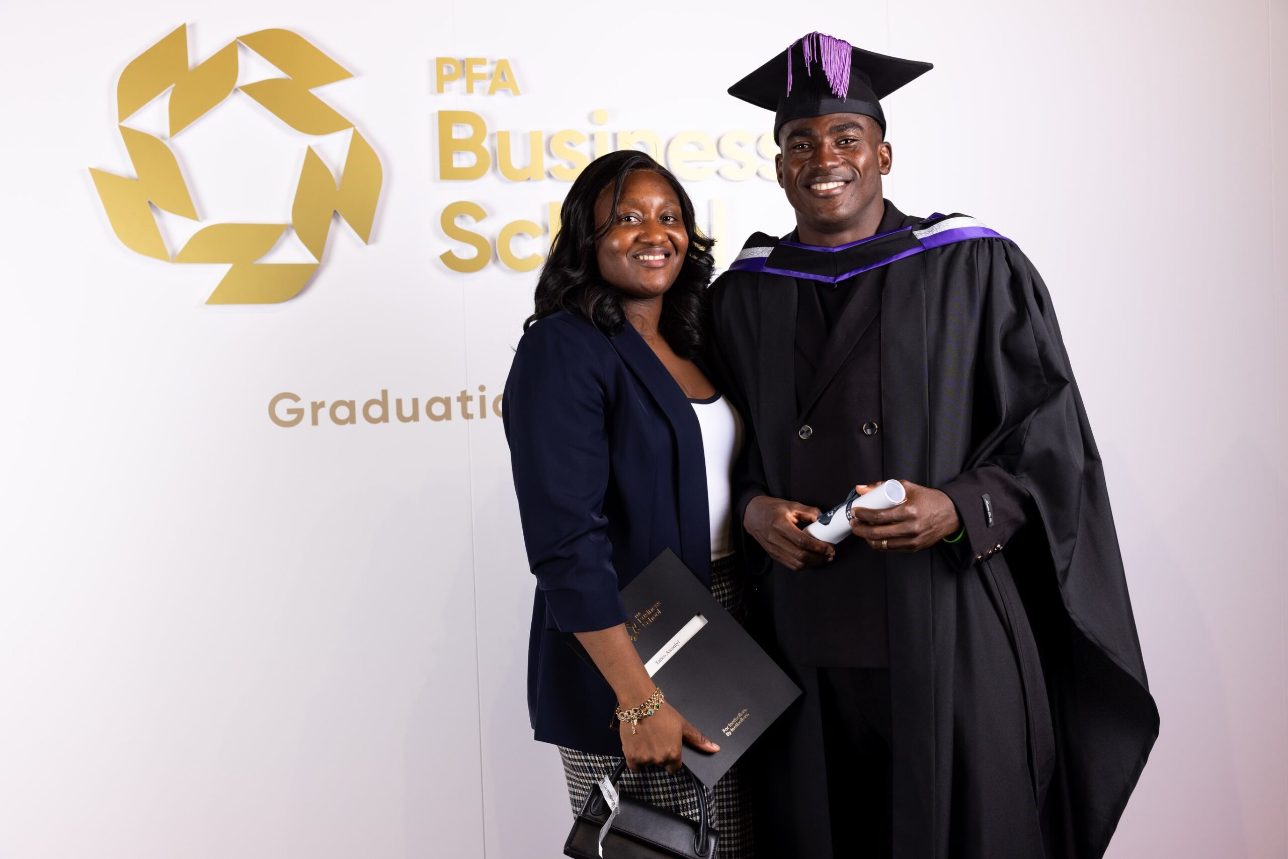 Taiwo Awoniyi in academic gown holding a diploma scroll beside his wife Taiye Jesudun at the PFA Business School graduation
