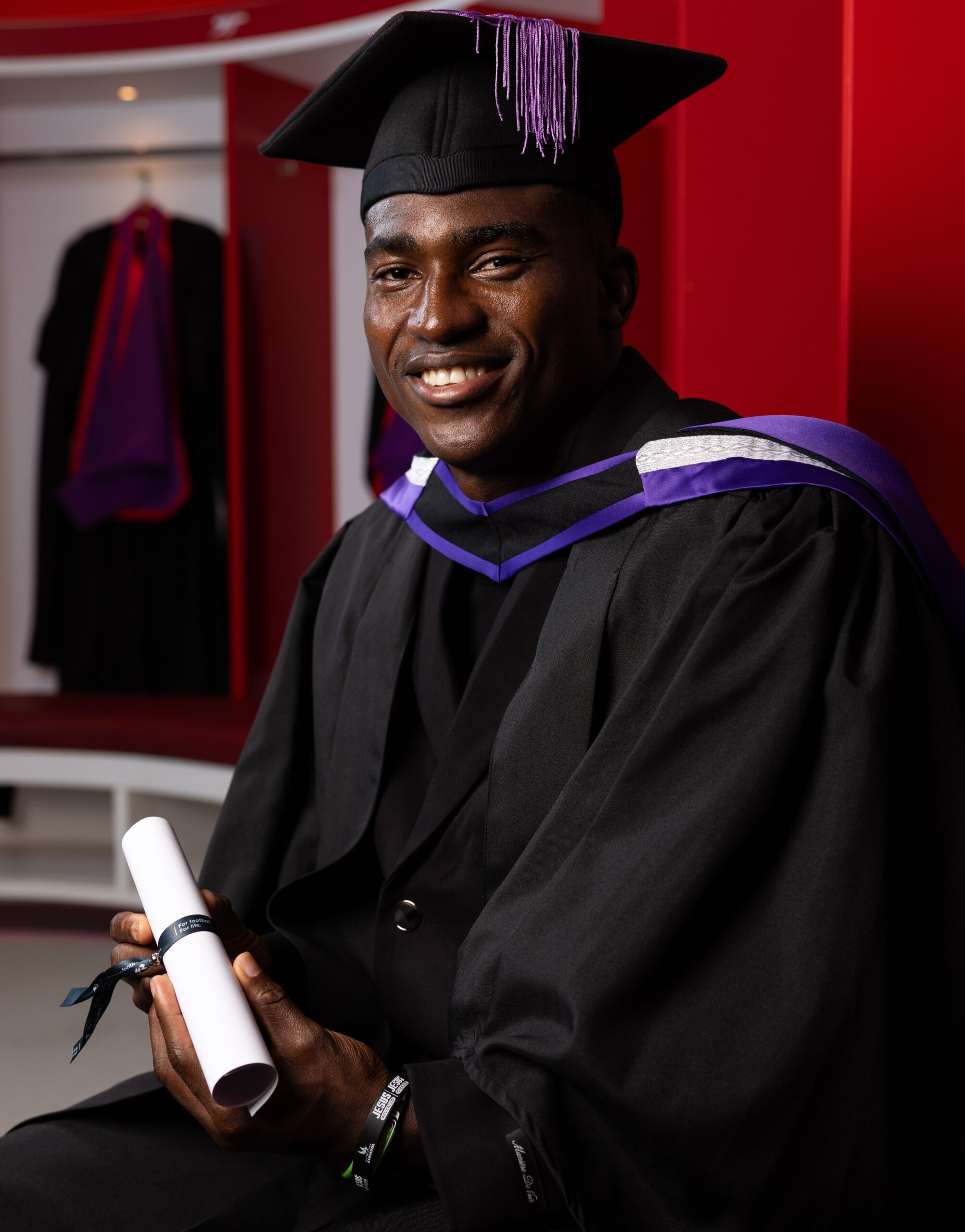 Taiwo Awoniyi seated in a dark gown and mortarboard holding his rolled graduation certificate