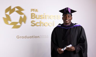Taiwo Awoniyi smiling in academic cap and gown holding his diploma scroll in front of the PFA Business School graduation logo
