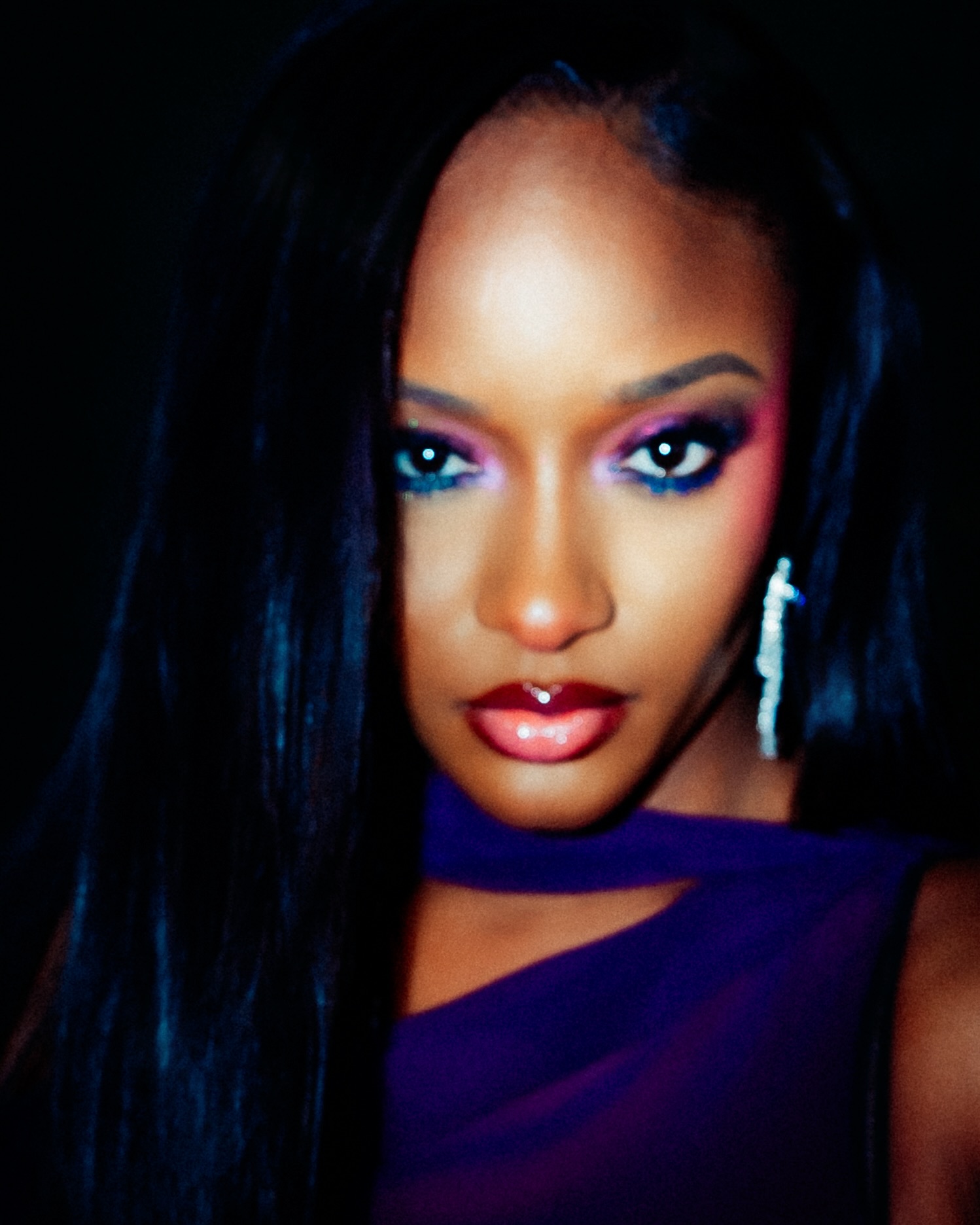 Ayra Starr wearing magenta and purple cut-crease eyeshadow with a high-shine glossy ombre lip and drop earrings.