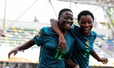 Two Nigeria Falconets players smiling and running side-by-side with arms around each other to celebrate a goal.