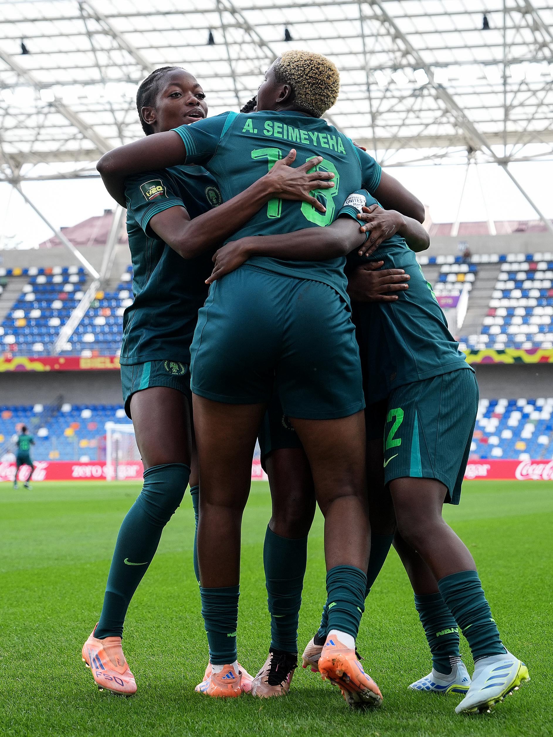 Nigeria Falconets players embracing in a group hug on the pitch to celebrate a goal against England.