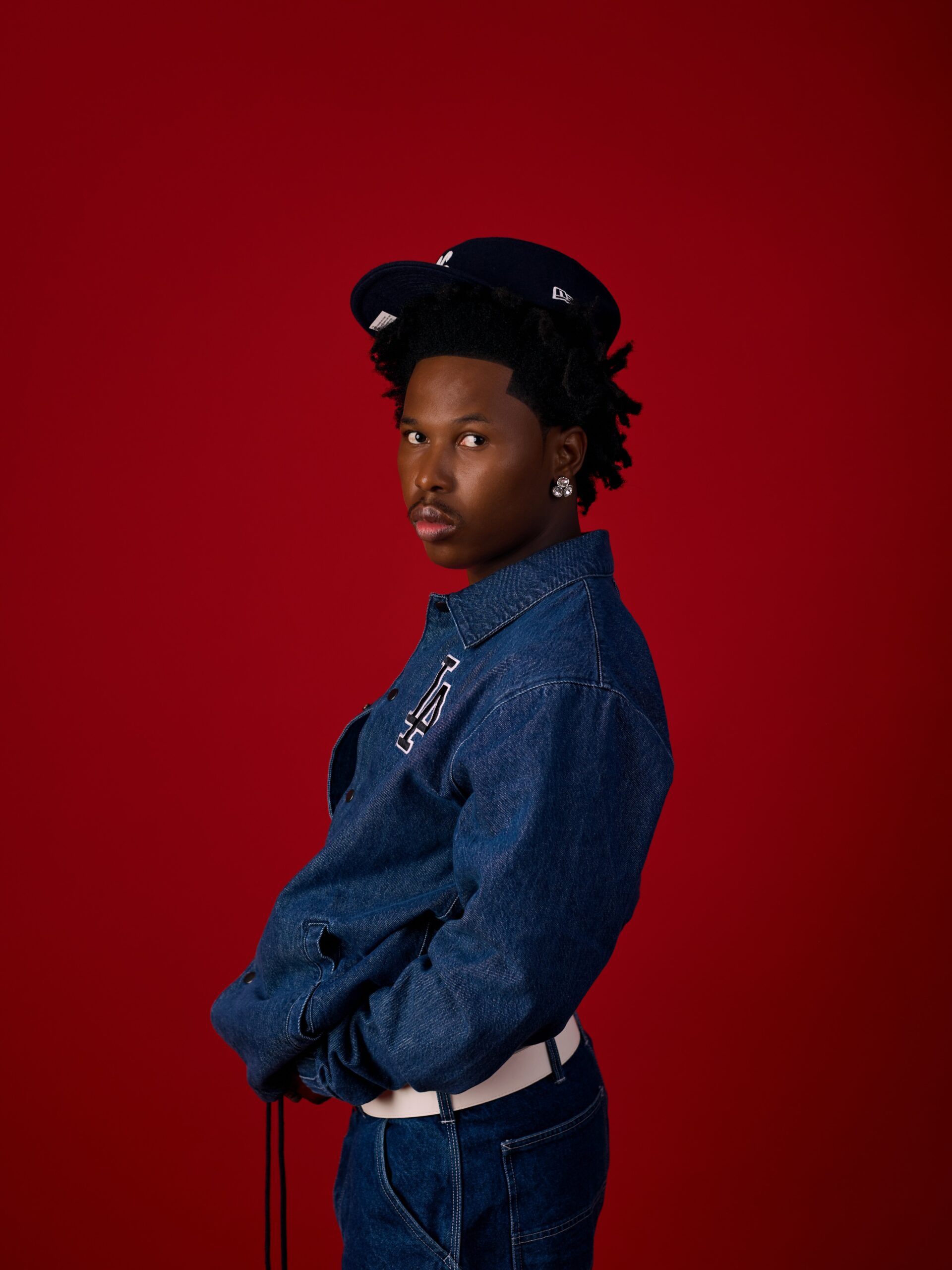 Shoday wearing a blue denim jacket and cap against a red background