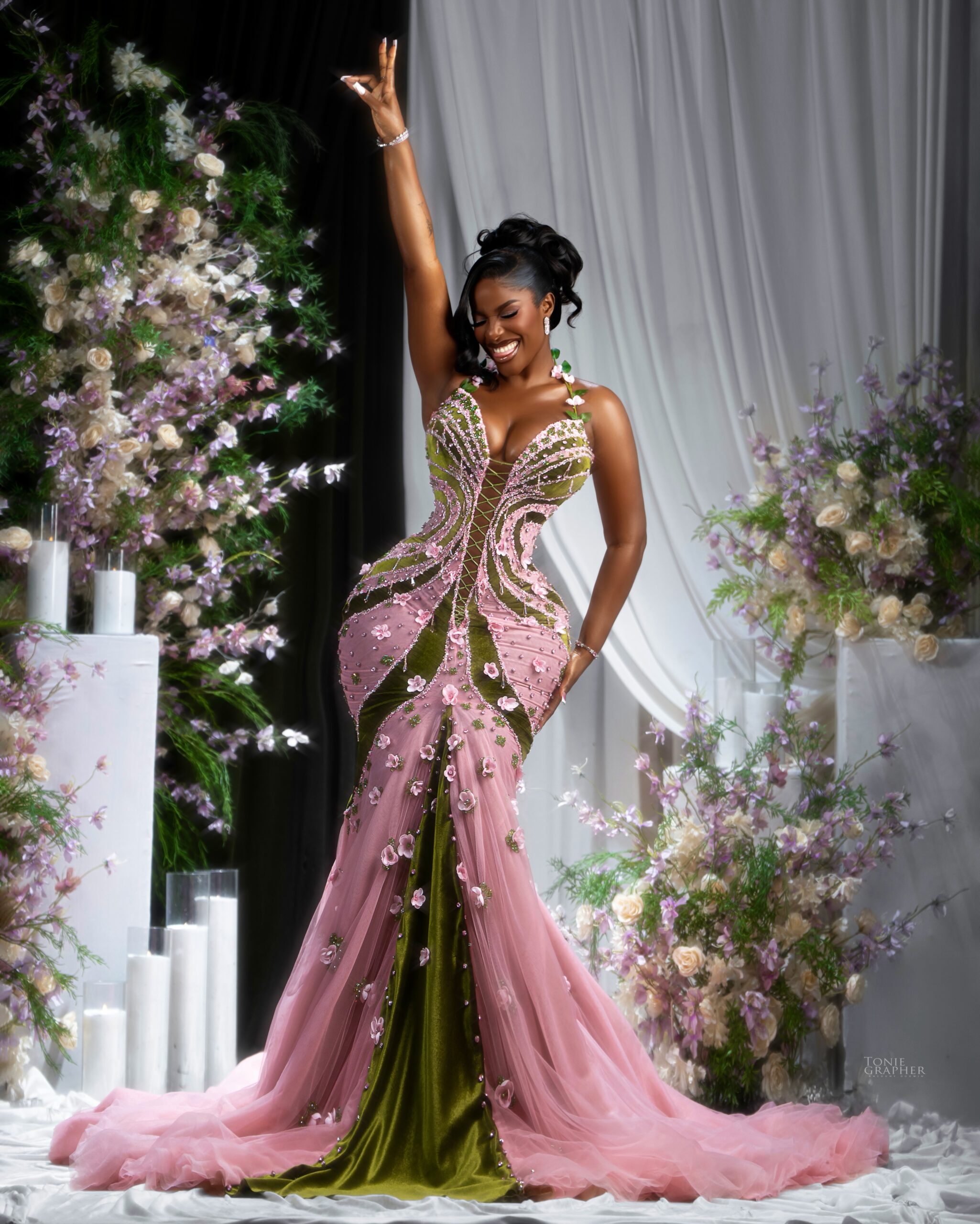 Hilda Baci raising one arm in celebration while wearing a pink and olive green corseted floral gown.