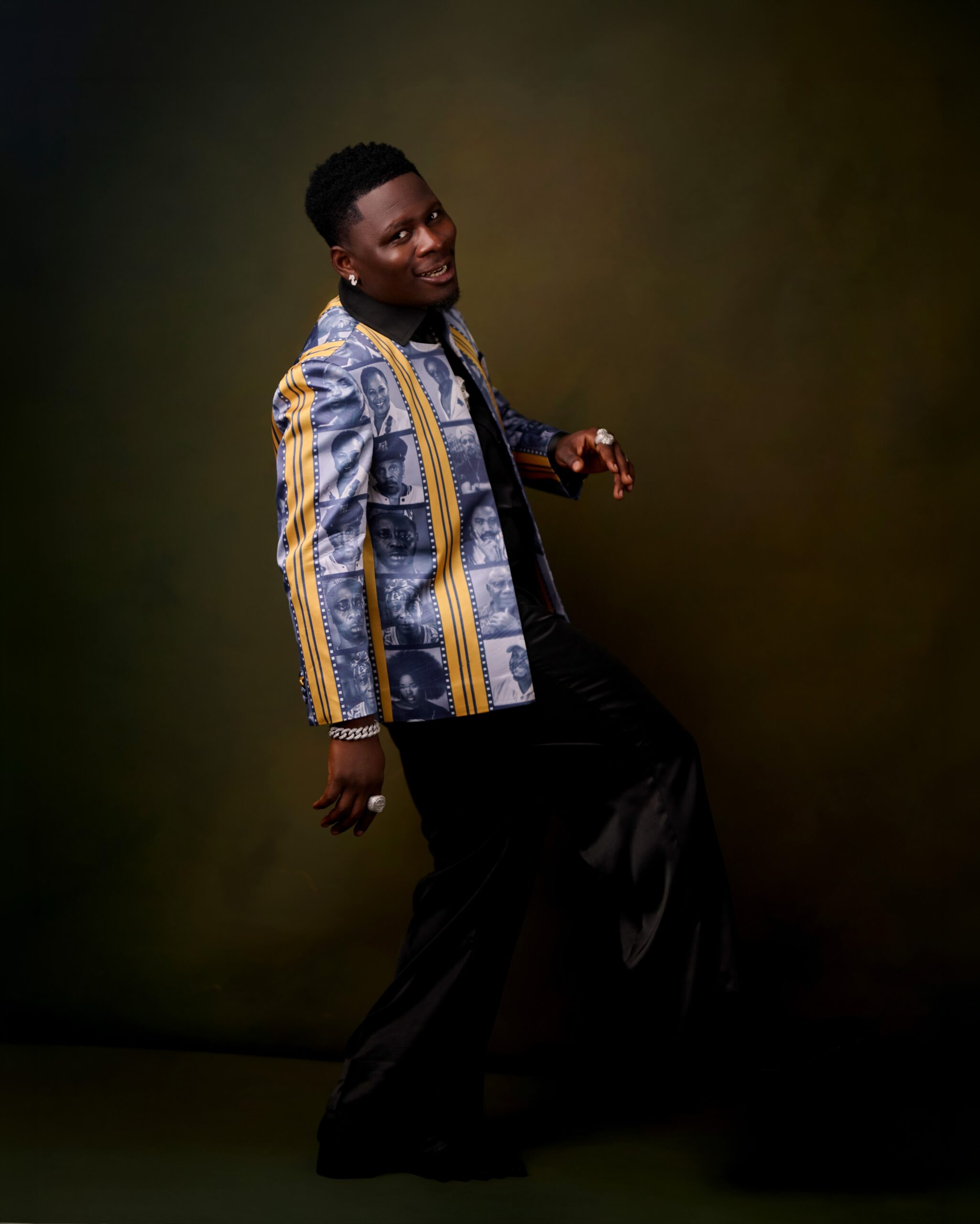 Akinyoola Ayoola, known as Kamo State, wearing a graphic film strip blazer and black wide-leg trousers at the Starlomo premiere.