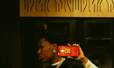 Shoday holding a phone displaying the title of his song CHE in a music studio