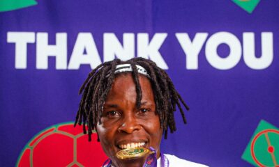Osinachi Ohale smiling while holding her WAFCON gold medal in front of a Thank You backdrop