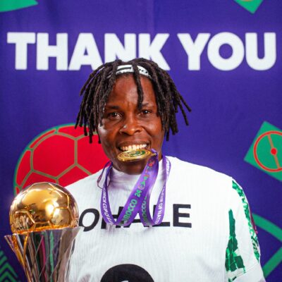Osinachi Ohale smiling while holding her WAFCON gold medal in front of a Thank You backdrop