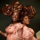 Veekee James and Tomike Adeoye smiling in peach sequin lace blouses, bronze-gold metallic headties, and warm bronzed makeup