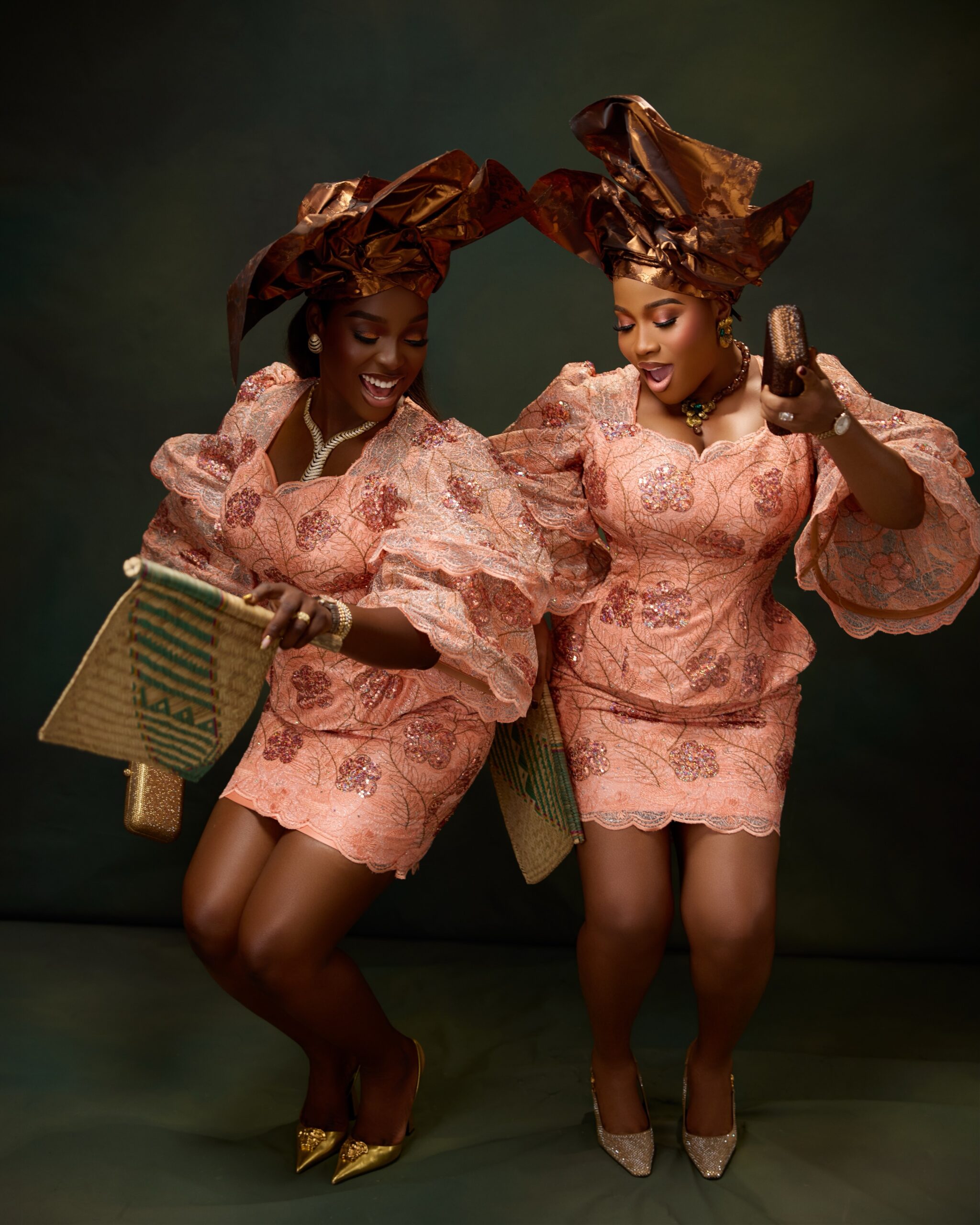 Veekee James and Tomike Adeoye dancing in peach embroidered lace blouse and skirt sets with bronze-gold fan headties