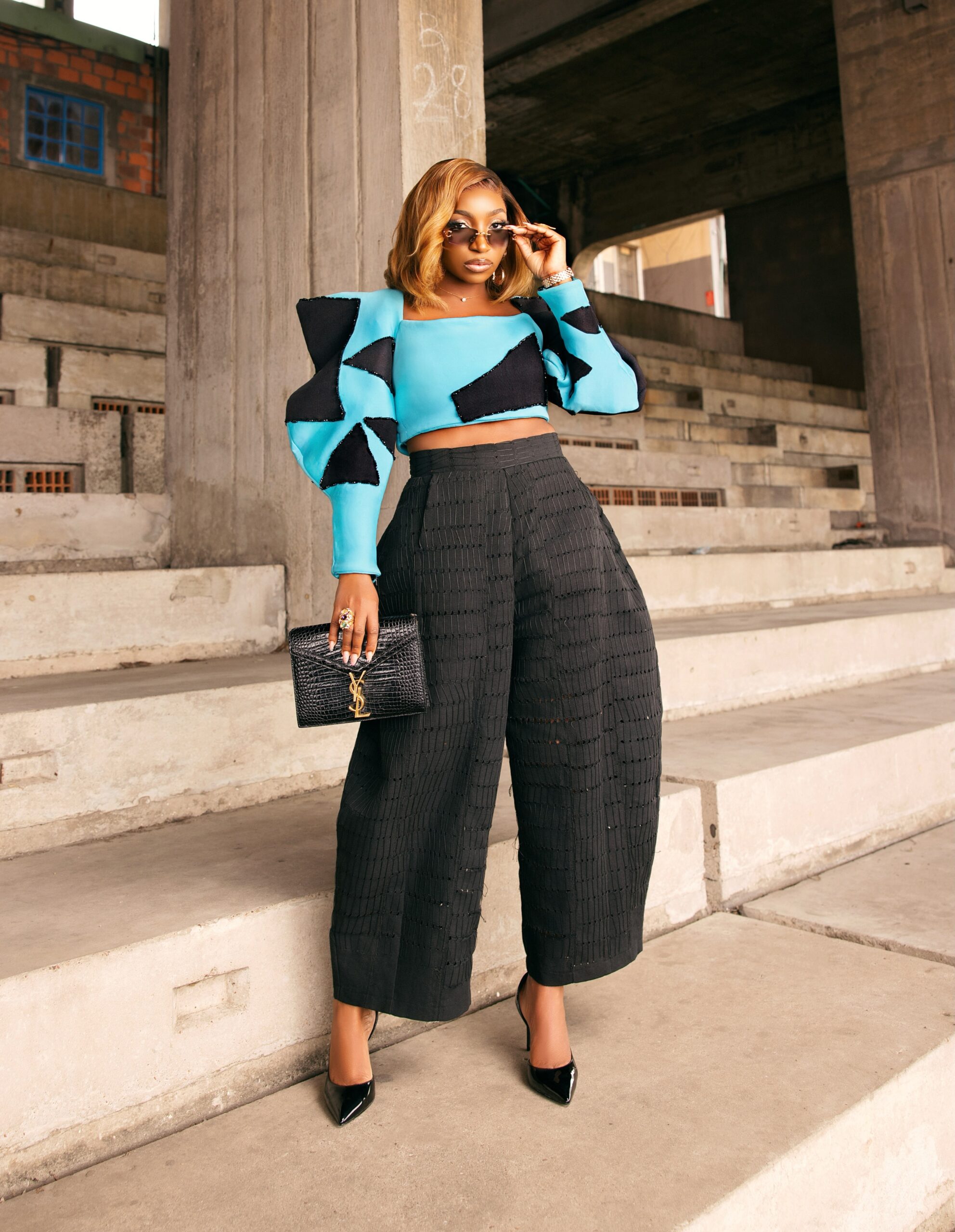 Omowunmi Dada holding a black crocodile-embossed YSL clutch bag and wearing rectangular sunglasses at the Black Market premiere