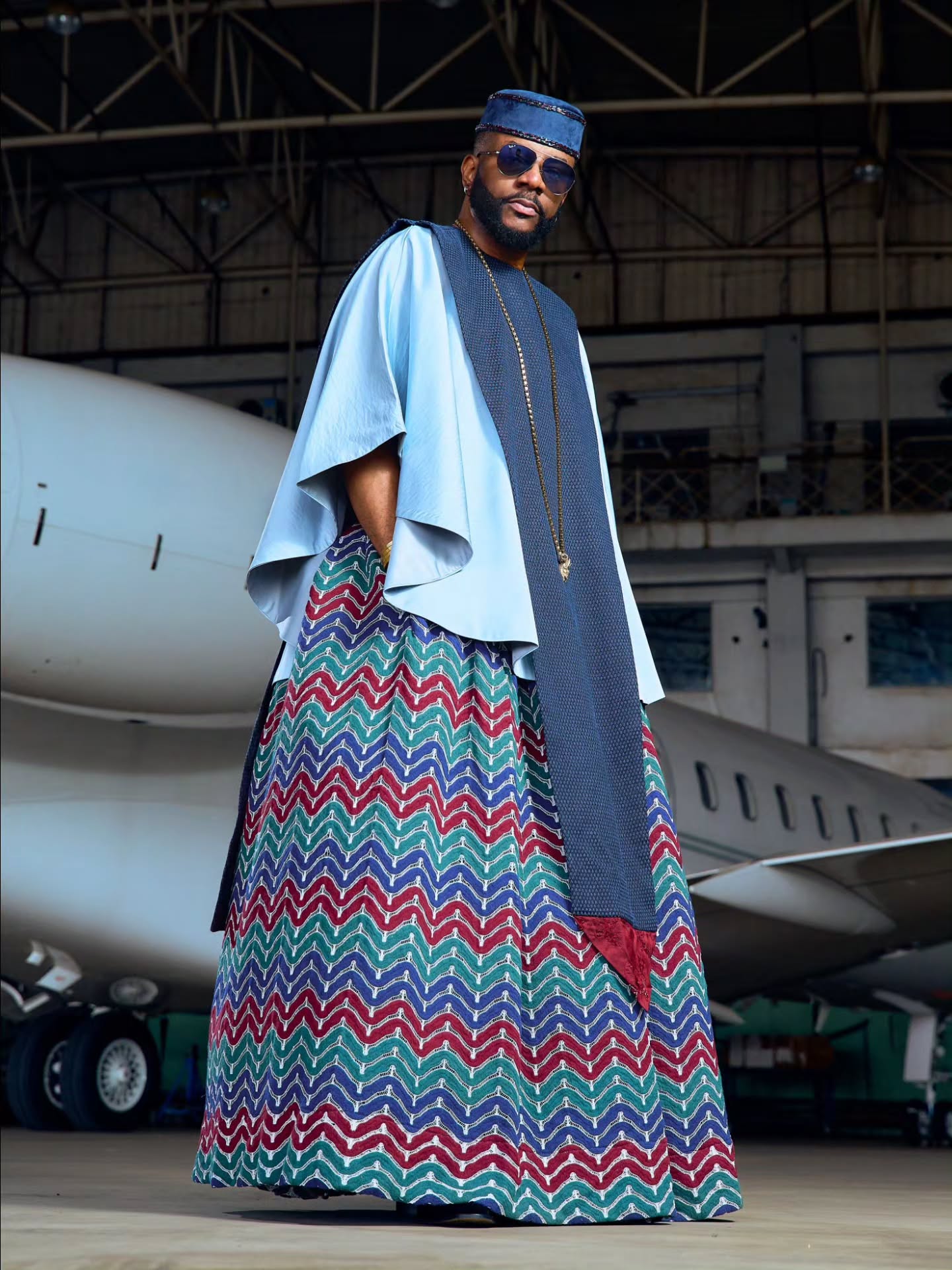 Ebuka Obi-Uchendu in a side-profile pose wearing wide-leg chevron print trousers and a sky-blue tunic in a hangar.