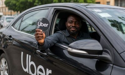 An Uber driver holding an Uber logo sign from inside a black vehicle in Nigeria