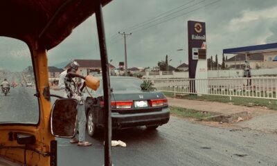 A man fills petrol from a container into a car by a Rainoil station, on a rainy street.