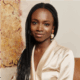 Yinka Ogunbiyi founder of HaloBraid wearing long box braids, statement drop earrings, and a champagne satin blouse.