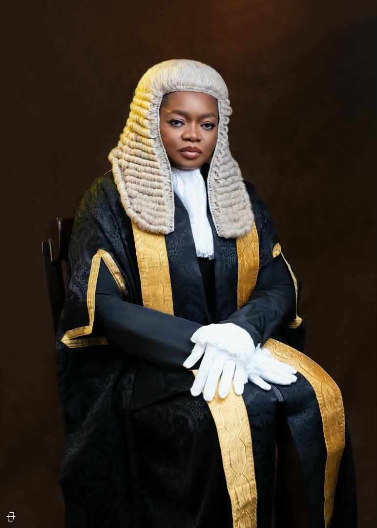 Olamide Ehinfun-Adekunle SAN wearing a legal wig, white lace-cuffed gloves, and black silk robe with gold embroidery while seated.