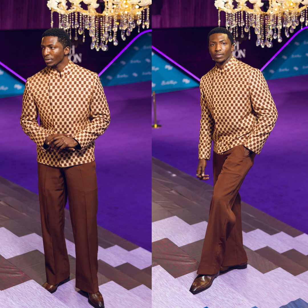 Shamz Garba in a brown and beige checkerboard mandarin collar jacket and brown wide trousers at BellaNaija red carpet.