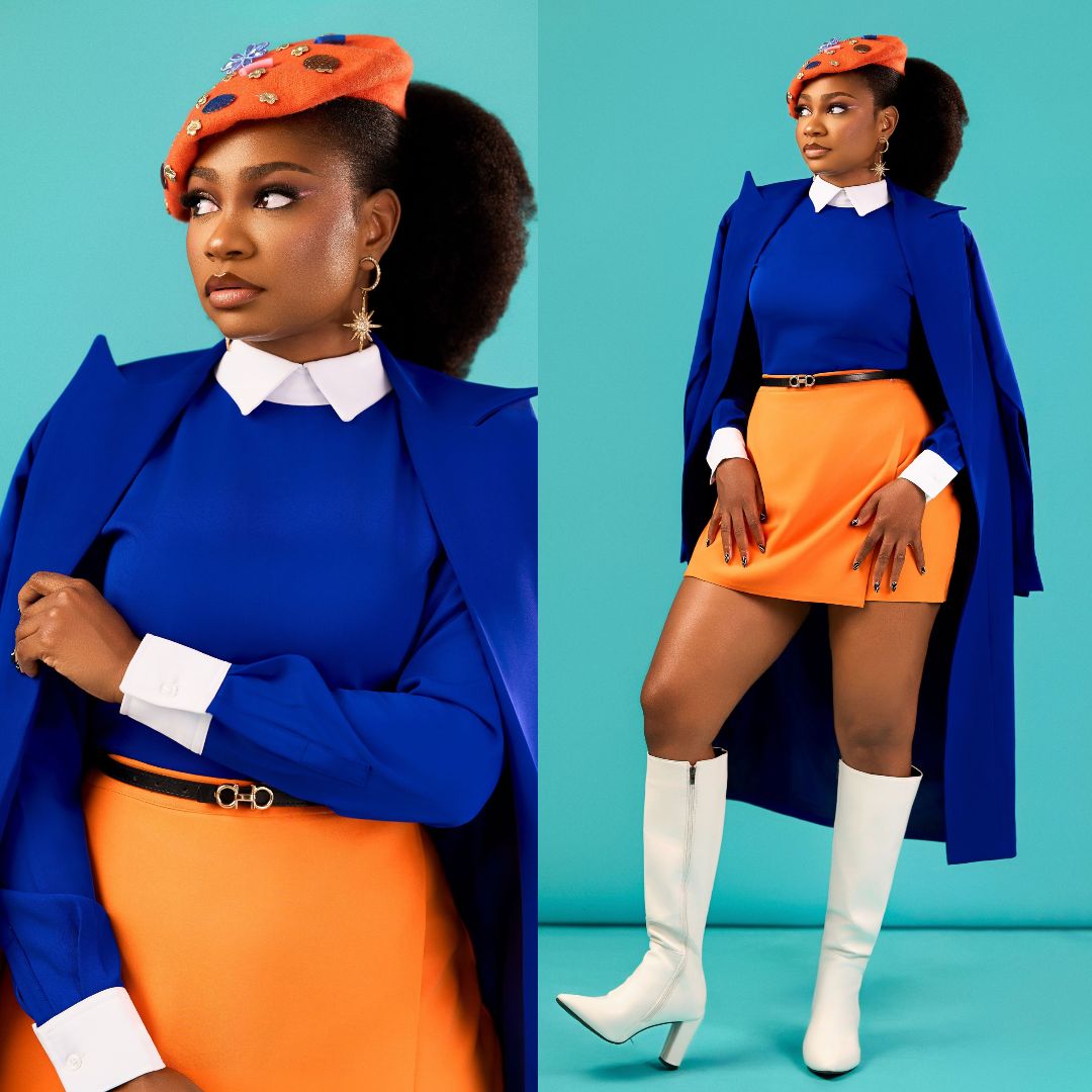 Sophia Chisom wearing a royal blue longline coat, burnt-orange wrap mini skirt, orange beret, and white knee-high boots.