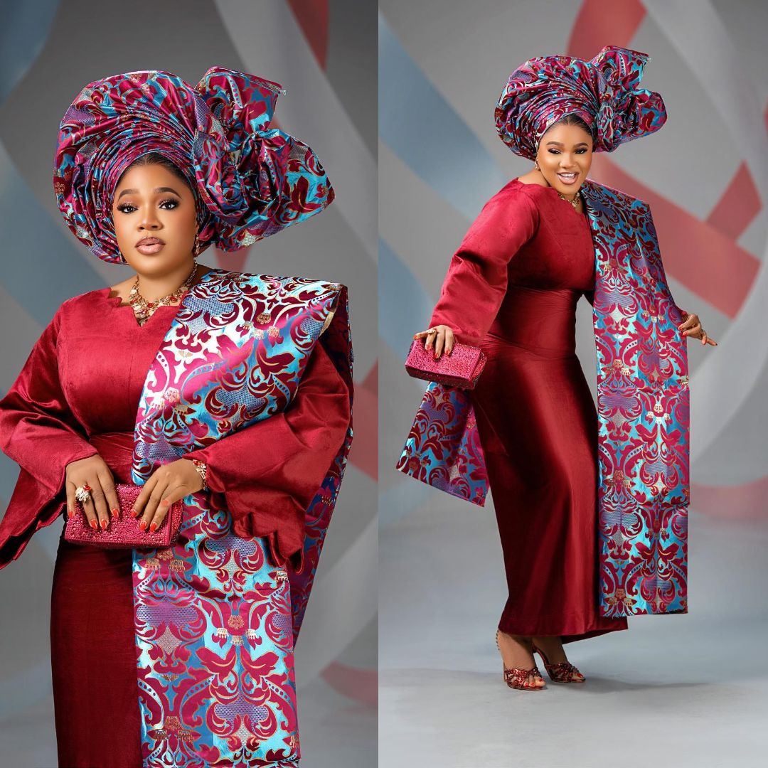 Toyin Abraham Ajeyemi wearing a crimson velvet floor-length gown with a patterned teal and magenta damask ipele and matching fan gele.