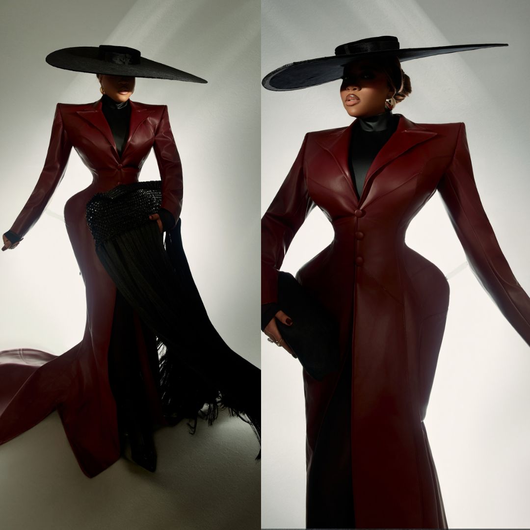 Veekee James in custom oxblood leather coat gown with exaggerated hips and saucer hat at BellaNaija 20th Anniversary Grand Red Carpet Experience.