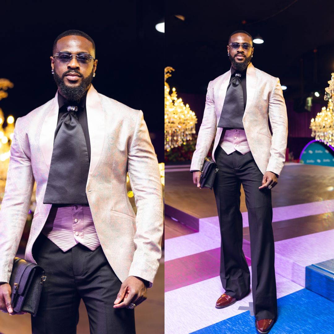 Yemi Cregx in an iridescent blush jacquard blazer, pleated waist vest, black high collar shirt, and wide leg trousers.