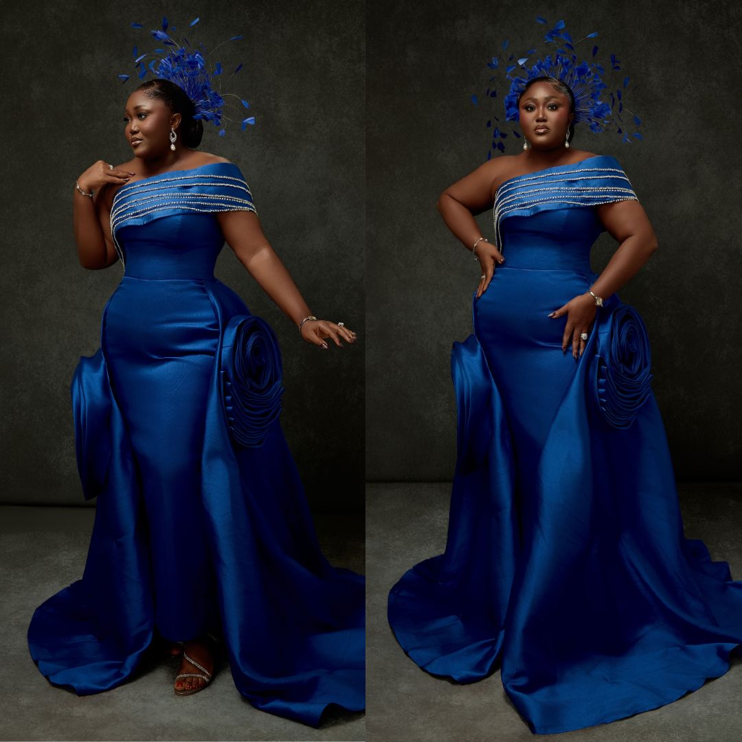 Blessing Nze in royal blue off-shoulder gown with pearl chest trim and feather fascinator at BellaNaija 20th Anniversary Grand Red Carpet Experience.