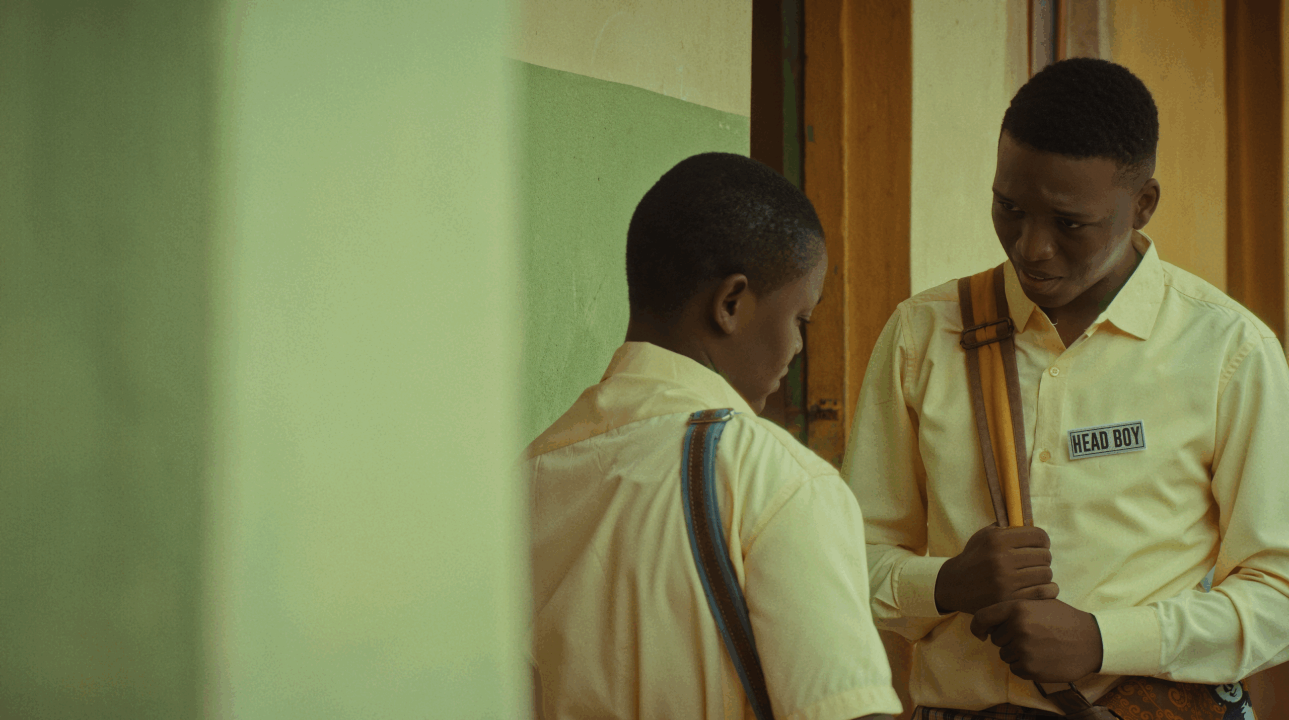 Adeoluwa Akintoba wearing a Head Boy badge conversing with another student in Her Daughters Mother.