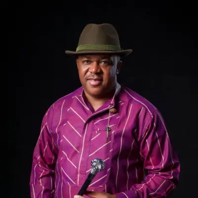 Veteran Nollywood actor Francis Duru wearing a purple striped traditional shirt, fedora hat, and holding a walking stick.