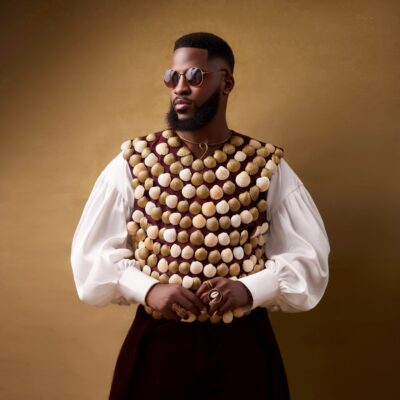Dr Akin Faminu wearing Mekallia cowrie-shell encrusted vest over billowy white shirt with round sunglasses for The Devil Wears Prada 2 Lagos premiere.