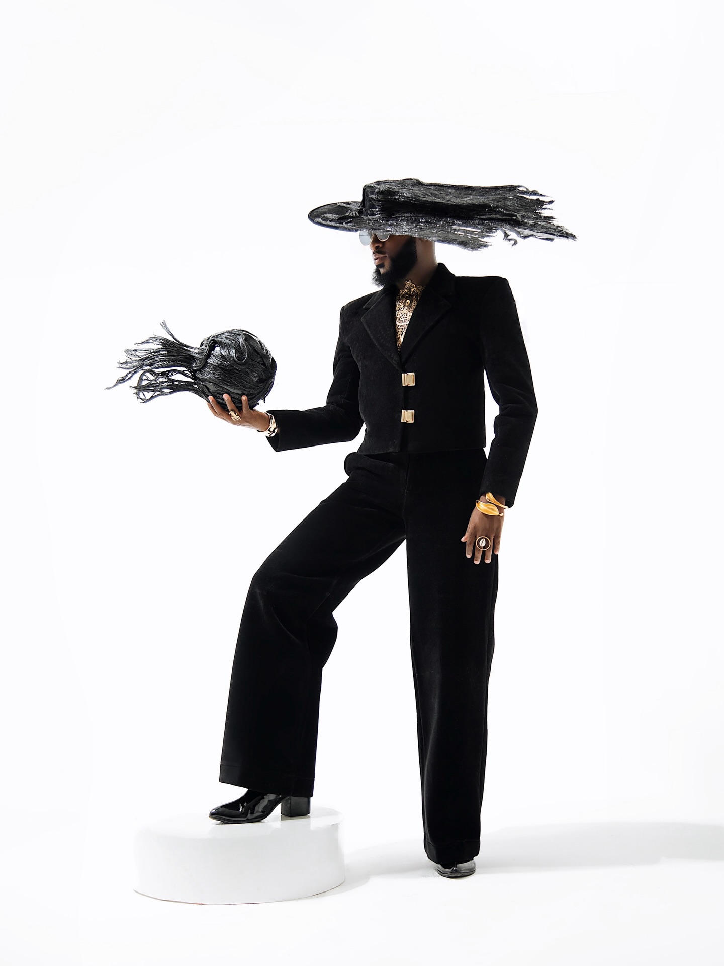 Akin Faminu wearing black Weiz Dhurm Franklyn SS26 structured jacket set with sweeping wind-sculpted brim hat and matching sphere accessory.
