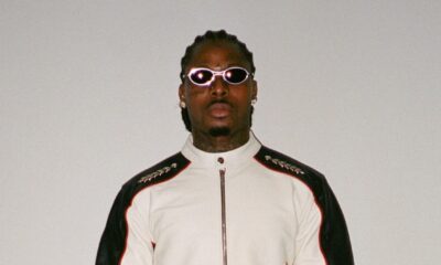 Asake wearing a white and black leather biker suit with oval sunglasses reflecting his Mr Money persona.