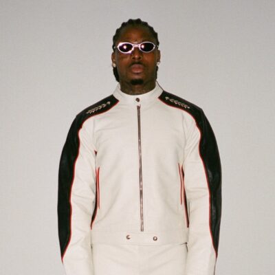 Asake wearing a white and black leather biker suit with oval sunglasses reflecting his Mr Money persona.