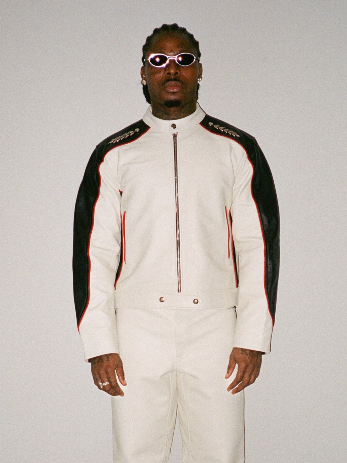 Asake wearing a white and black leather biker suit with oval sunglasses reflecting his Mr Money persona.