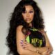 Cardi B posing in a printed graphic outfit with long wavy hair and blue nails.
