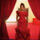 Uche Pedro standing in a custom crimson red ruffled trumpet dress at BellaNaija Grand Red Carpet Experience.