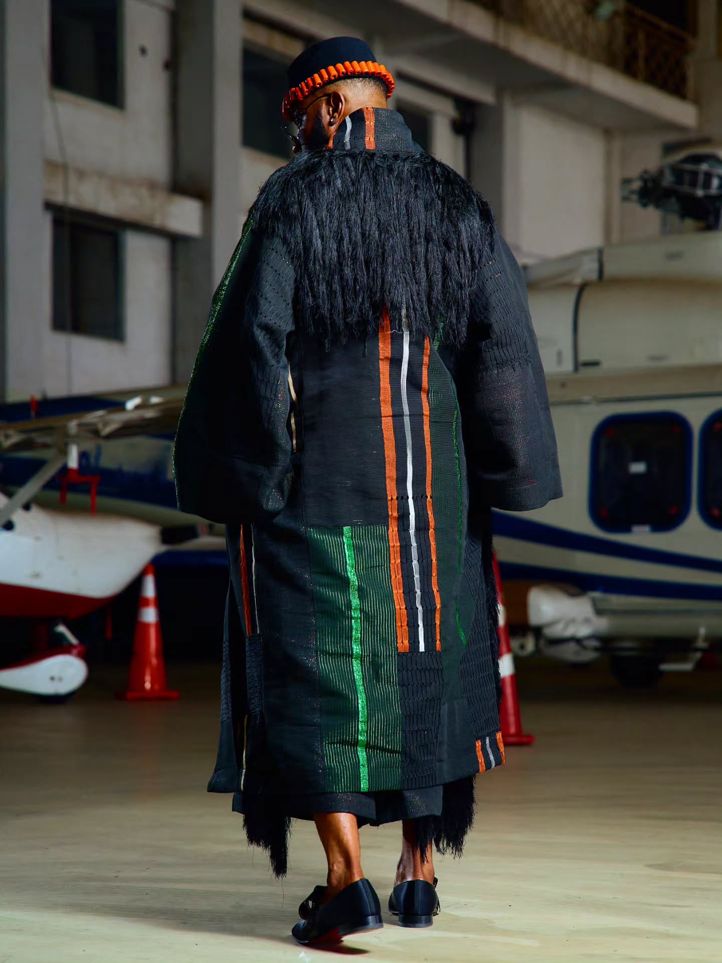 Ebuka Obi-Uchendu showing the rear fringe yoke and metallic woven stripes of his long black Atafo coat.