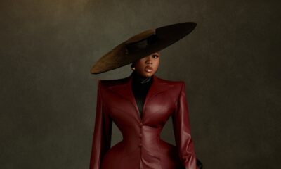Veekee James wearing an oxblood leather coat-gown by Abbas Woman with structured shoulders, peplum hips, a wide-brim hat, and pointed heels at the BellaNaija at 20 Grand Red Carpet Experience.