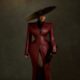 Veekee James wearing an oxblood leather coat-gown by Abbas Woman with structured shoulders, peplum hips, a wide-brim hat, and pointed heels at the BellaNaija at 20 Grand Red Carpet Experience.